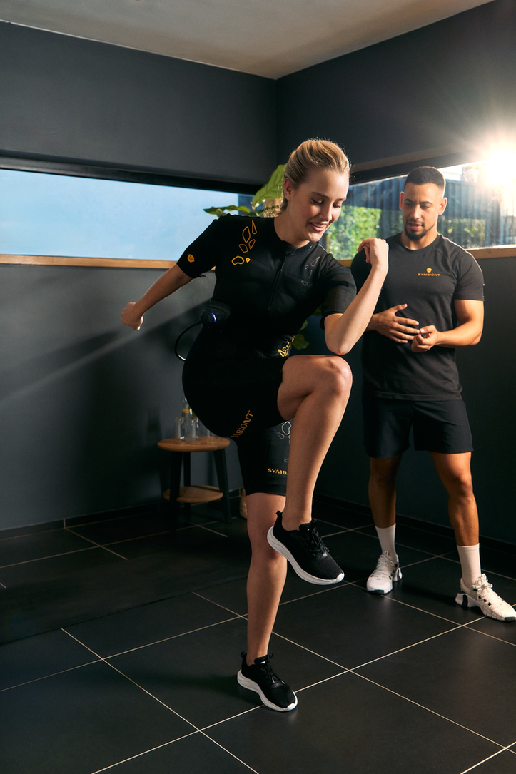 Doświadcz Treningu SYMBIONT EMS w Toim Lokalnym Studiu EMS Trener personalny prowadzący klienta w kombinezonie SYMBIONT EMS podczas sesji próbnej w lokalnym studio EMS. Doświadcz spersonalizowanego treningu, wsparcia i motywacji podczas swojej sesji próbnej EMS.