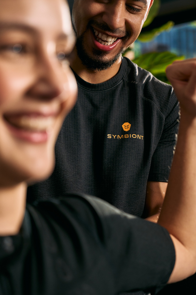 Zbliżenie klienta i trenera personalnego omawiających cele treningowe i fitness w lokalnym studio EMS, aby zapewnić najlepsze doświadczenie treningowe z SYMBIONT.